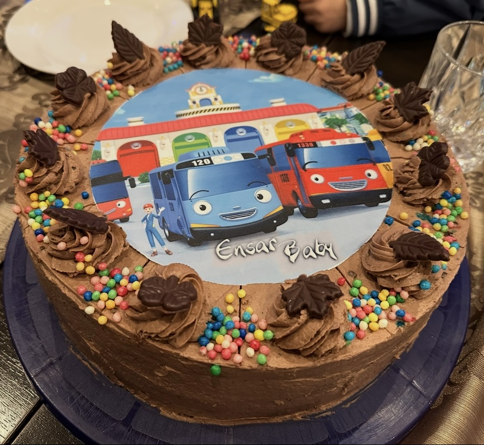 Round chocolate photo cake with a colourful bus design and sprinkles