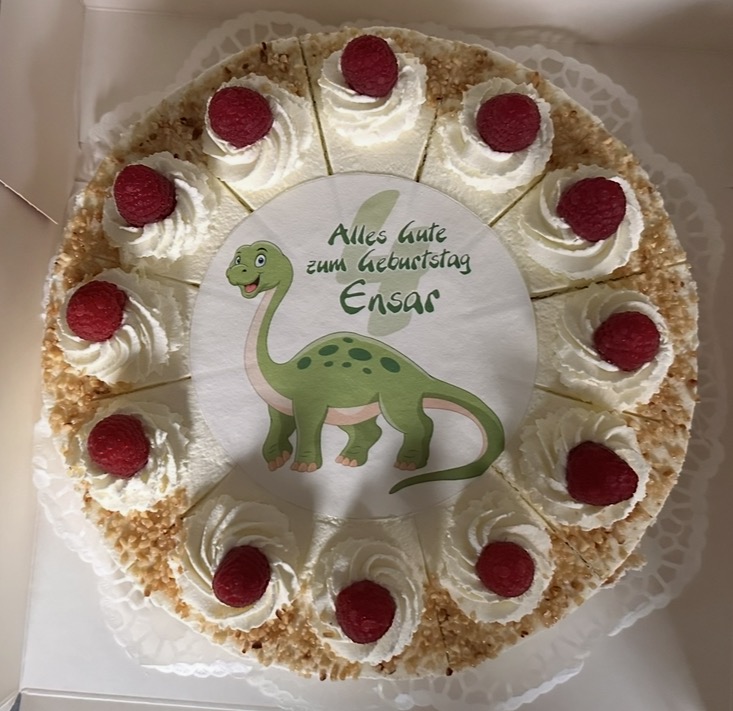 Round birthday cake with a dinosaur design and raspberries